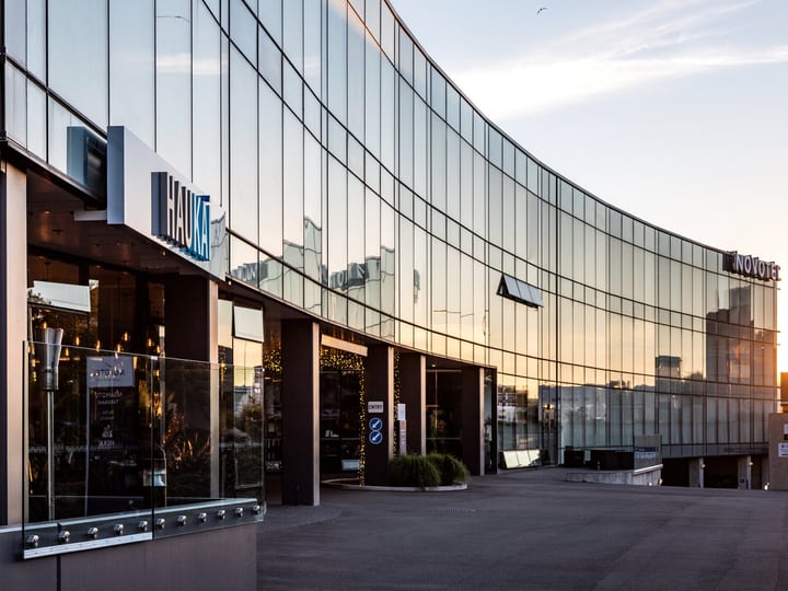 Curved glass-facade building exterior with dark columns and signage at sunset