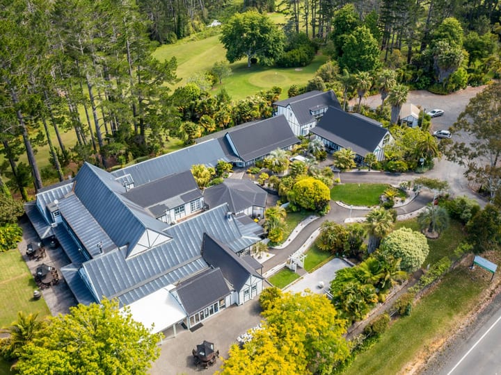 Aerial view of lodge complex with pitched roofs surrounded by mature gardens