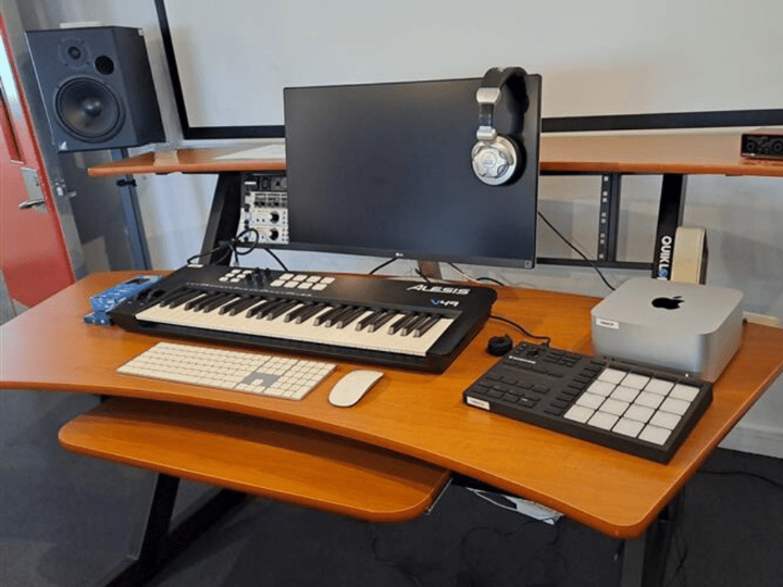 Recording studio desk with keyboard controller, monitor speakers, and screens