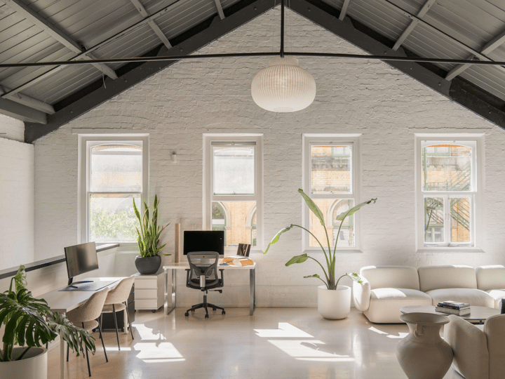 White-painted brick interior with vaulted steel-truss roof, lounge seating, desks, and tall plants