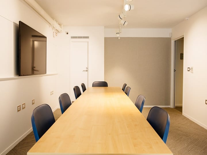 Small boardroom with long timber table and blue chairs, wall-mounted screen