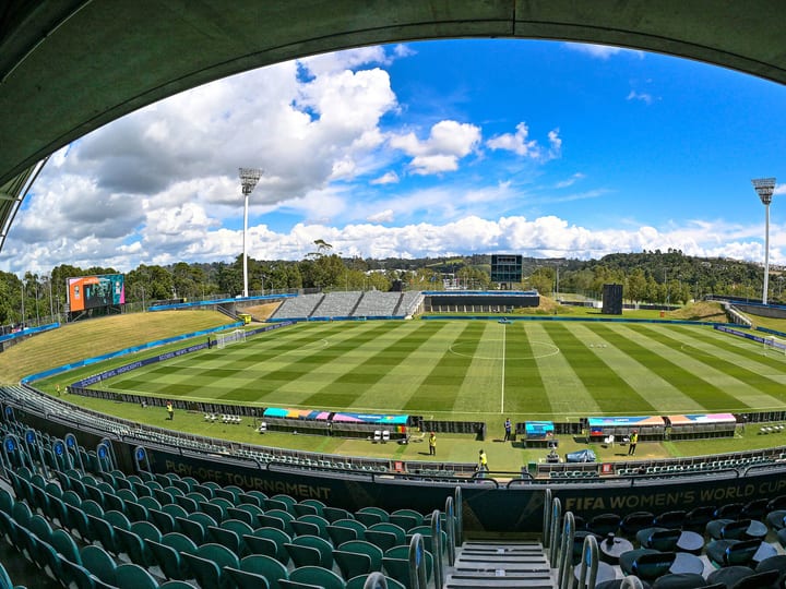 Empty stadium bowl with grass pitch and covered grandstands viewed from end