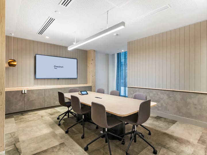 Meeting room with timber table, grey chairs, wall screen and vertical timber panelling, stone tile floor