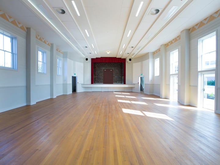Renovated hall interior with polished timber floor, raised platform with red curtain, and decorative ceiling