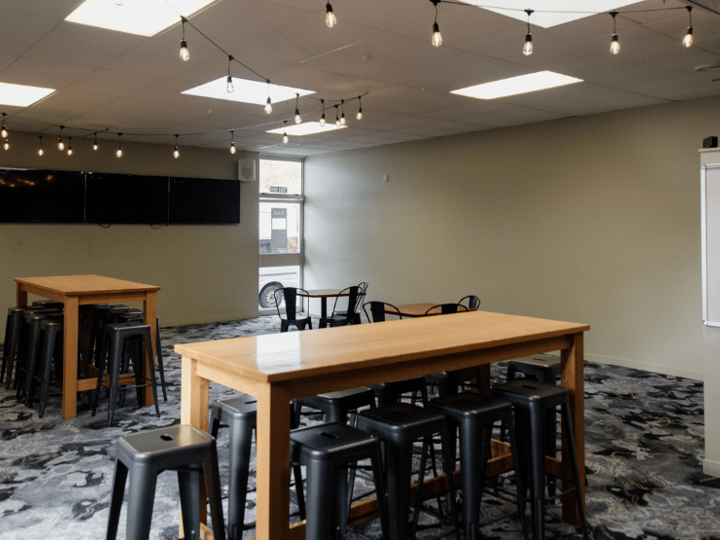 Bar area with high timber tables, bar stools, multiple screens and stone-faced pillars
