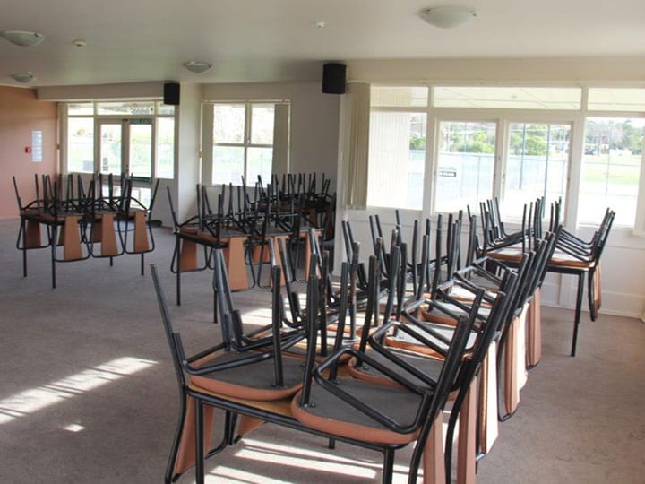 Hall with rows of stacked chairs and tables, windows along one side
