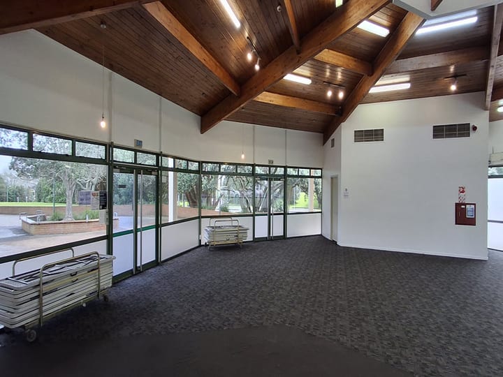 Hall with exposed timber roof beams, carpet floor and full-height glazed walls to grounds
