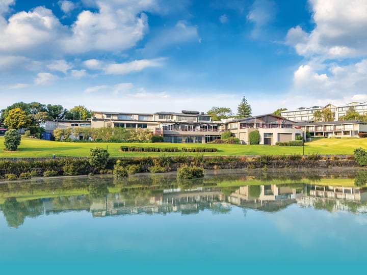 Multi-storey hotel complex reflected in still lake, surrounded by lawns and trees