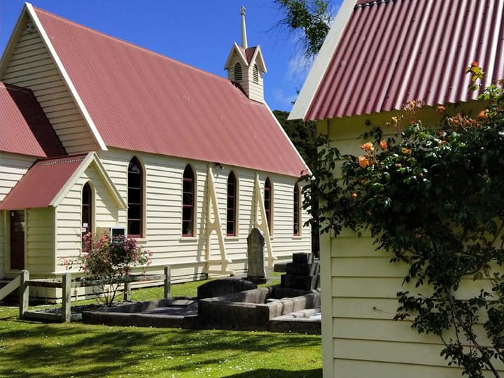 White timber church with red roof and gardens viewed from the side