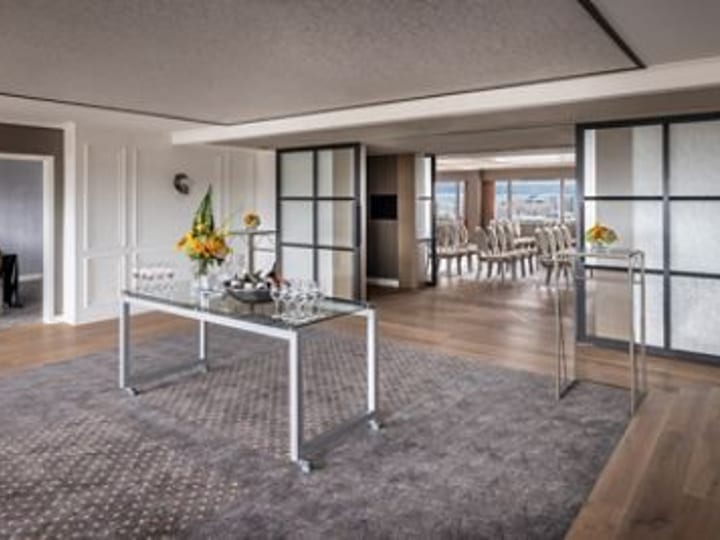 Hotel suite with lounge area, glass partition, and dining area beyond