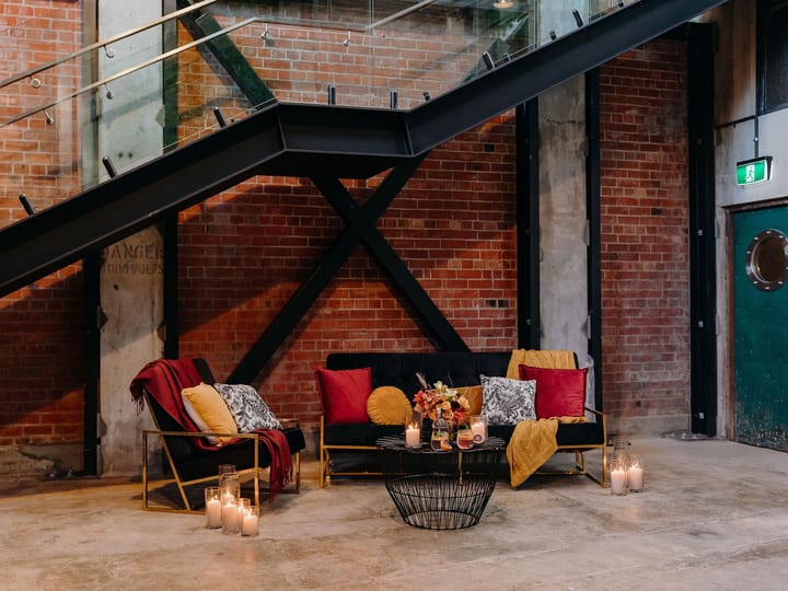 Lounge seating area with velvet sofas and candles beside exposed brick wall and steel staircase