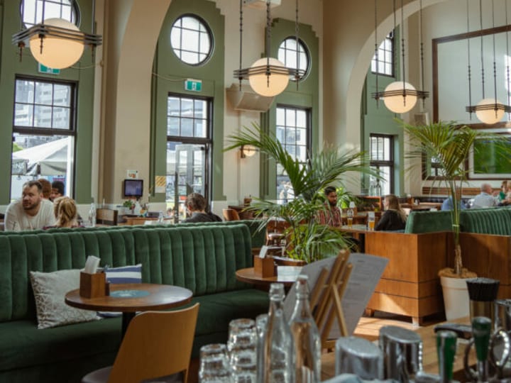 Backlit bar shelves with bottles under arched alcoves, timber counter, and tropical plants in the foreground