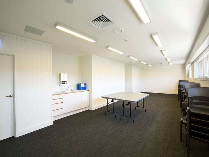Plain meeting room with dark carpet, small sink bench, and folding tables