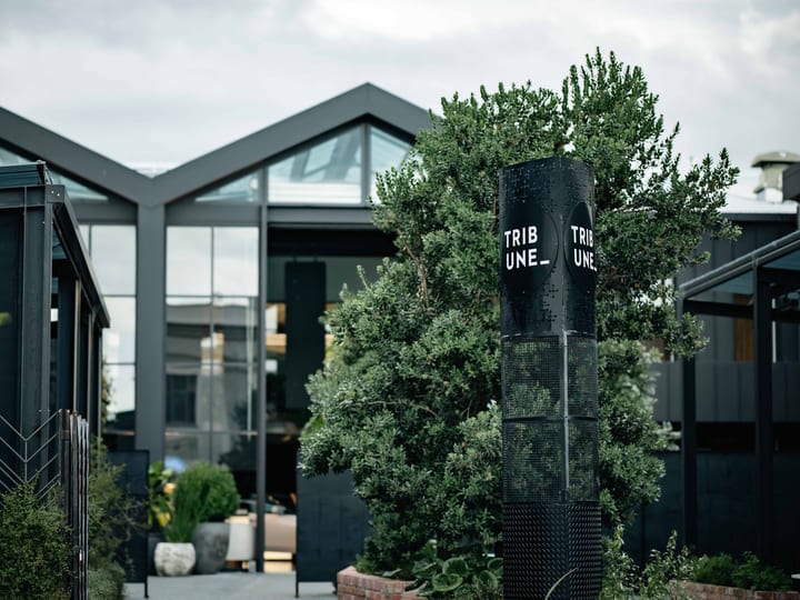 Dark-clad venue exterior with peaked gable glazing and branding signpost