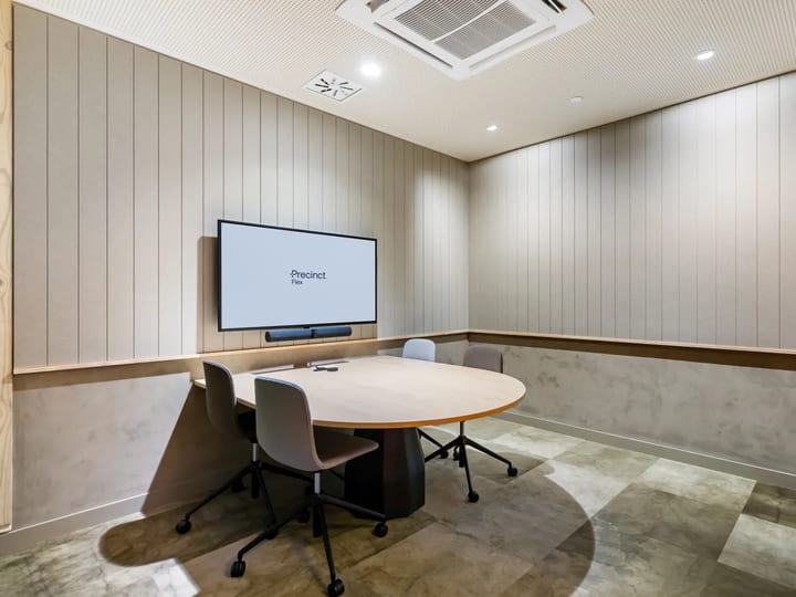 Small meeting room with oval table, grey chairs, screen and vertical timber wall panelling, stone floor