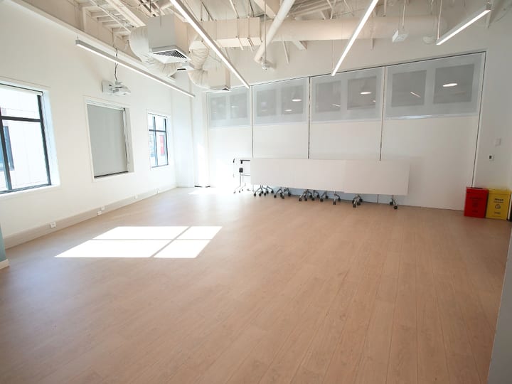 Flexible room with timber floor, folded tables on wheels, and projection screen