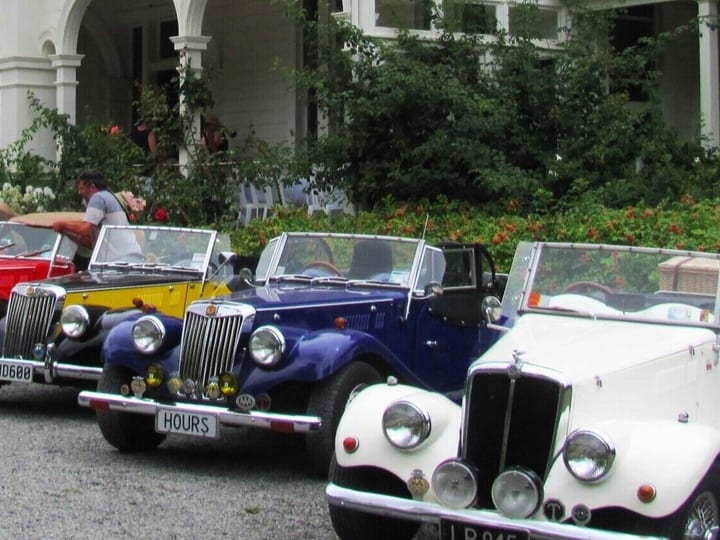 Row of vintage cars parked in front of heritage homestead