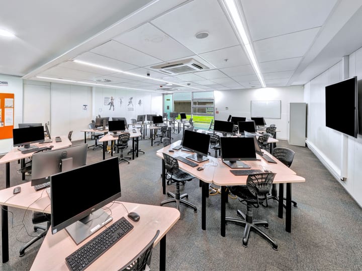Computer classroom with desktop workstations and wall-mounted screen
