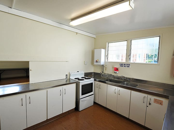Hall kitchen with white cabinets, stainless benchtops, stove and sink