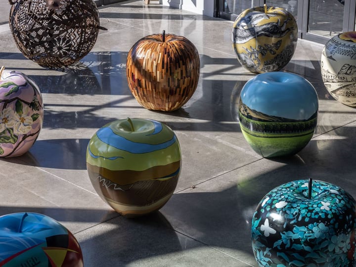 Large colourful apple sculptures displayed on polished concrete floor under glazed roof