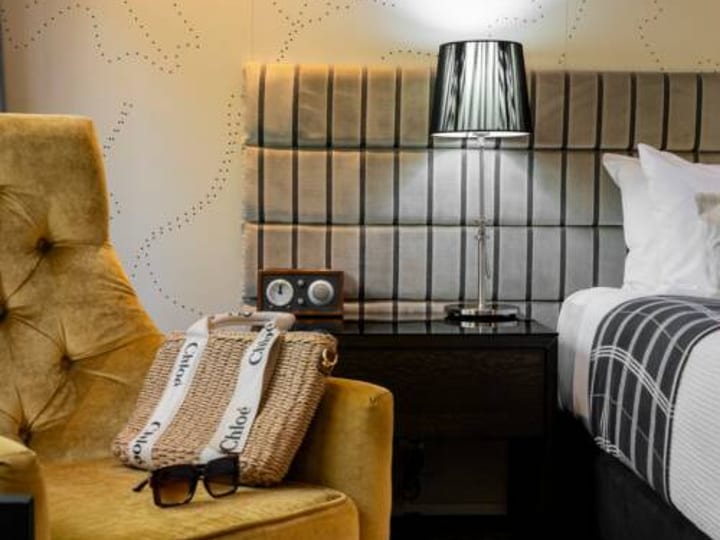 Mustard velvet armchair beside upholstered headboard, patterned wallpaper and bedside lamp