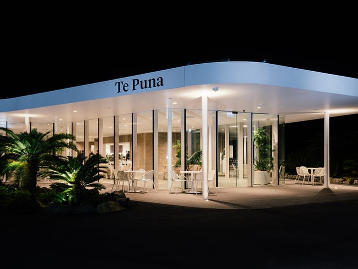 Modern curved building exterior illuminated at night with landscaping