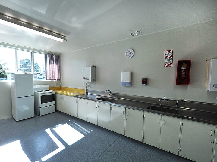 Plain community kitchen with white appliances and stainless steel bench