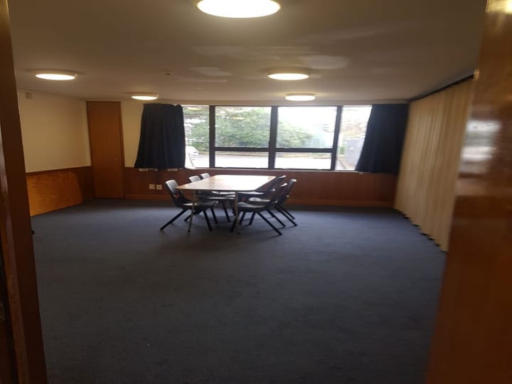 Small carpeted meeting room with central table, chairs and curtained windows