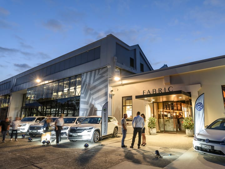 White rendered commercial building exterior at dusk with illuminated entrance and vehicles outside