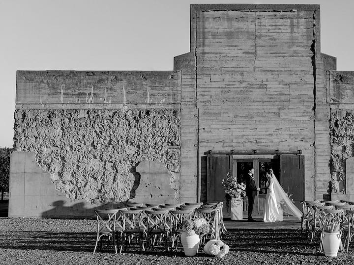 Rough concrete block building with stepped facade, rows of chairs set for outdoor ceremony