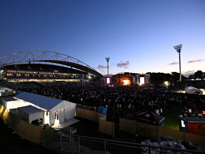 Stadium exterior at dusk with concert event and large crowd on field