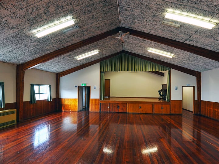 Hall interior with timber-beamed gable ceiling, polished floor, and raised platform with curtain