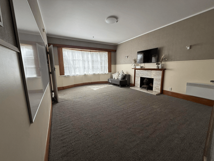 Carpeted lounge room with fireplace, sofa, and bay window