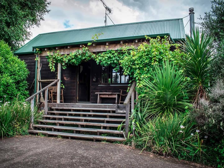 Dark timber cottage with covered verandah surrounded by lush garden