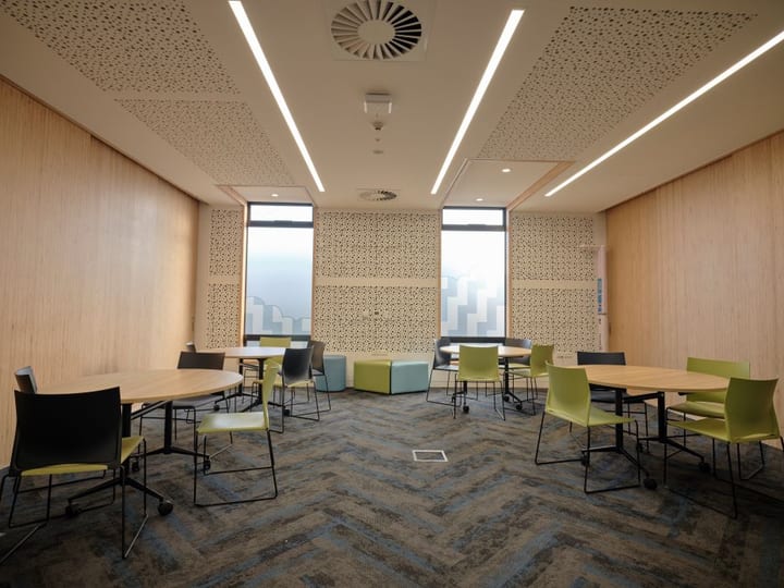 Modern room with timber walls, round tables, green and black chairs, and patterned carpet