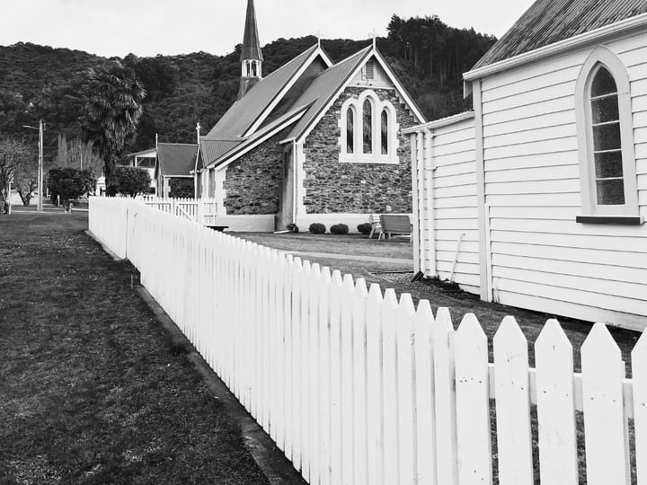 Black and white view of stone church buildings with white picket fence