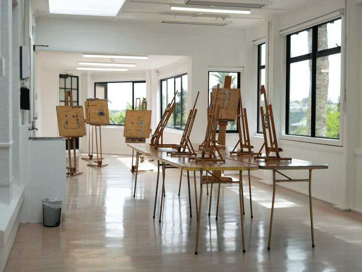 Bright studio room with multiple easels and large windows overlooking trees