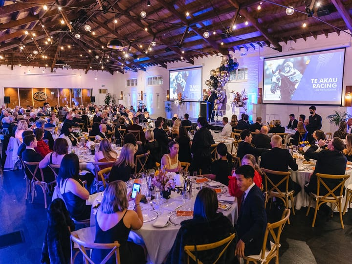 Full hall set for gala dinner with timber ceiling, festoon lights, and projected screen