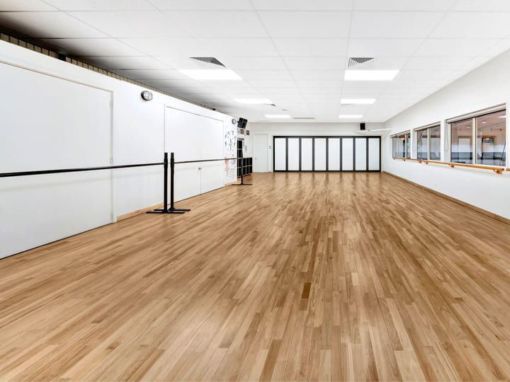 Long timber-floored room with wall-mounted barre rail, mirrors and folding partition doors
