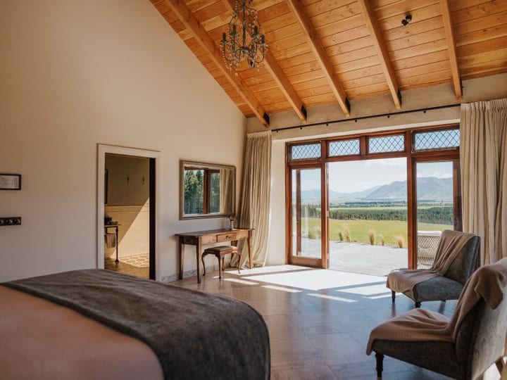 King bedroom with timber ceiling, glazed doors and mountain plain view beyond