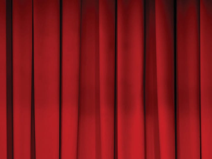 Deep red theatre curtain under stage lighting, close-up