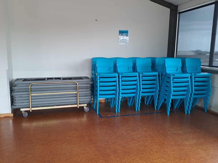 Room with stacked blue chairs and folded trestle tables on trolley