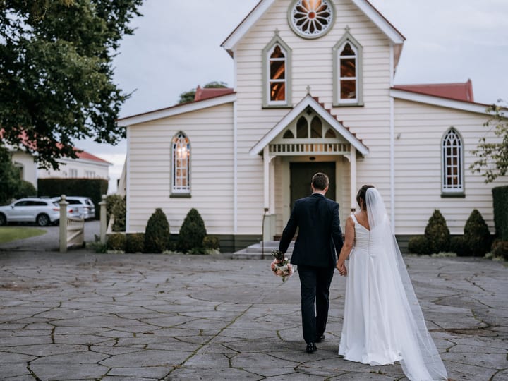 White timber church with gothic arched windows and red roof on paved forecourt