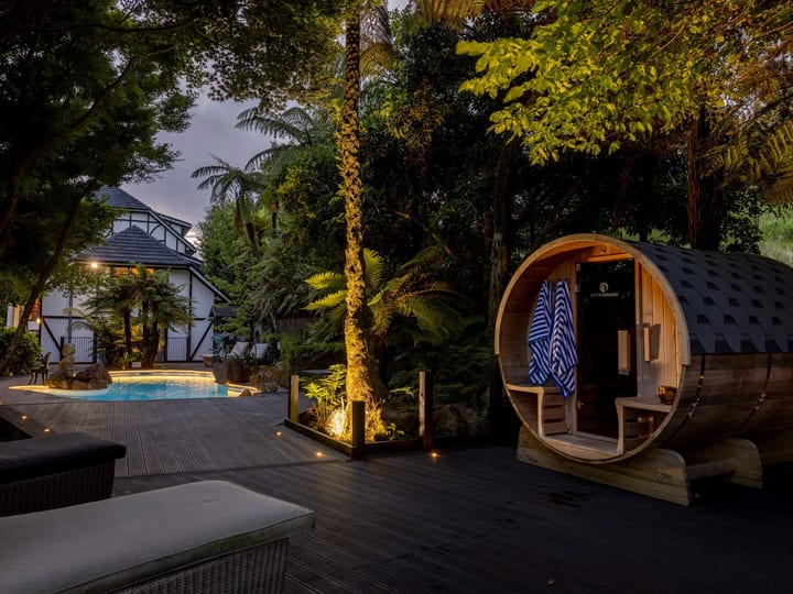 Deck area at night with barrel sauna, pool, and trees lit by ground lights