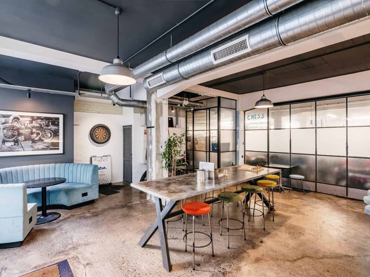 Industrial bar lounge with exposed ducting, concrete floor, bar-height table, and booth seating