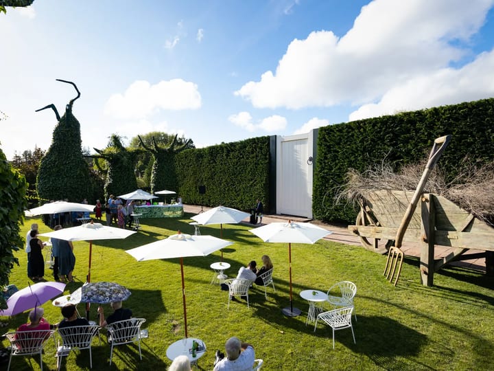Garden courtyard set for outdoor event with white market umbrellas and sculptural elements