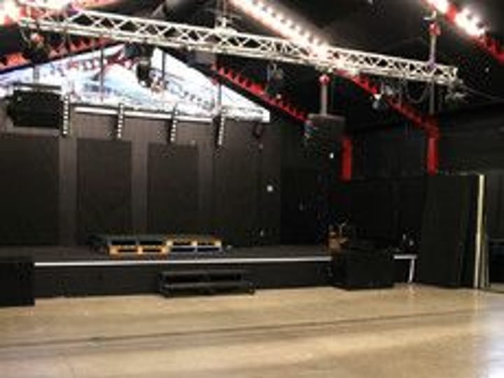 Industrial black venue hall with raised platform, truss lighting rig and concrete floor