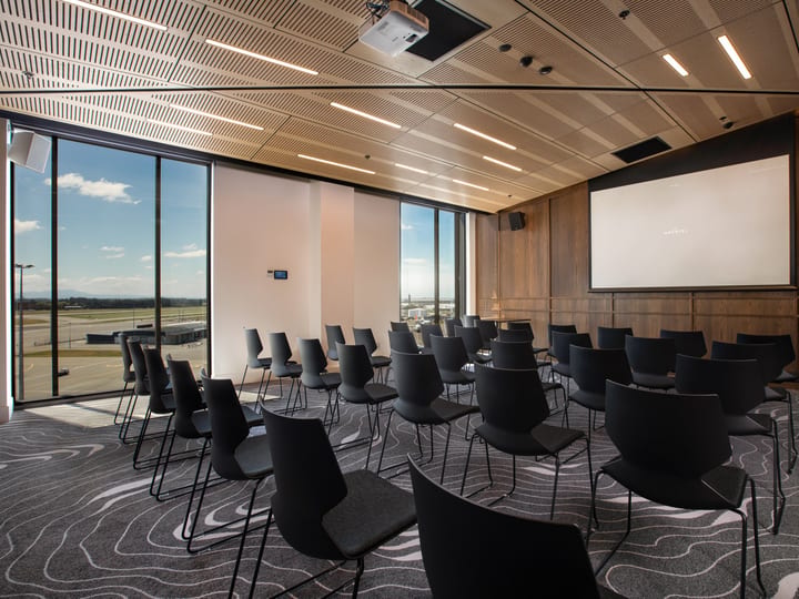 Timber-panelled meeting room with theatre seating, projection screen, and corner windows overlooking open ground