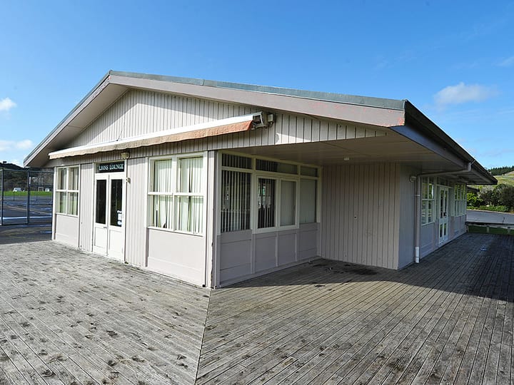 Single-storey weatherboard lounge building with deck on grass sports ground