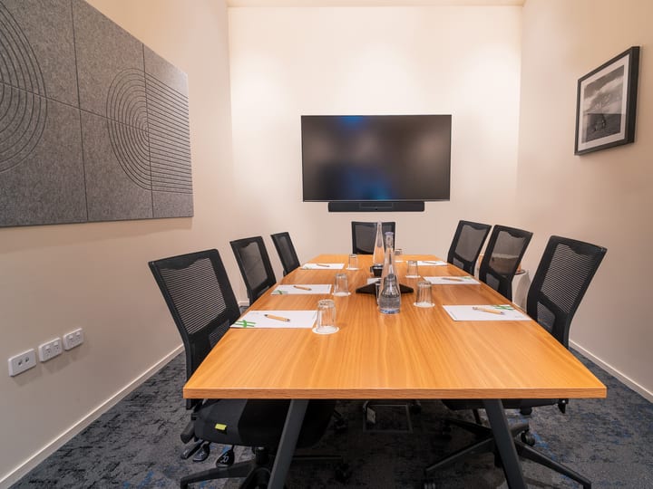 Boardroom with rectangular timber table, mesh chairs and wall-mounted screen